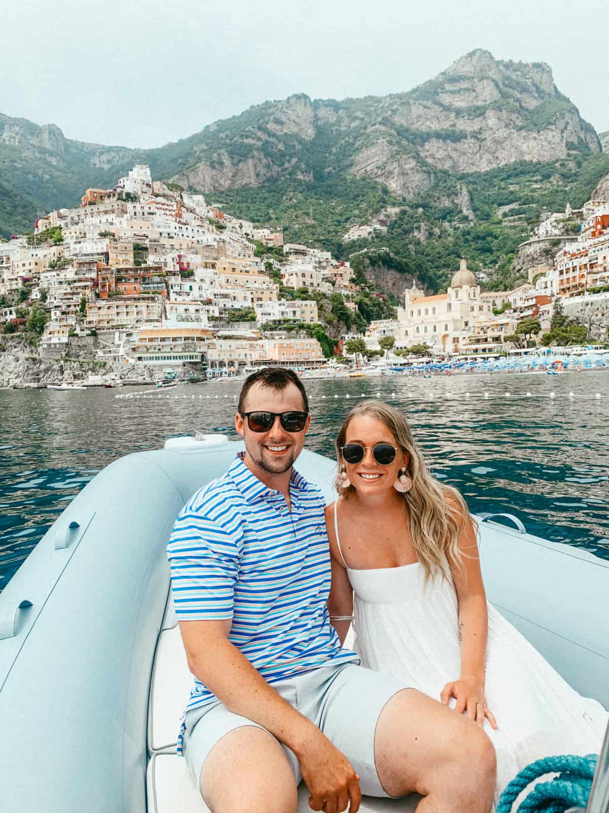 Abby and Sam on a boat in the Amalfi Coast with colorful building behind them. This trip is one of the reasons they created their couples travel blog Trekking Price's.