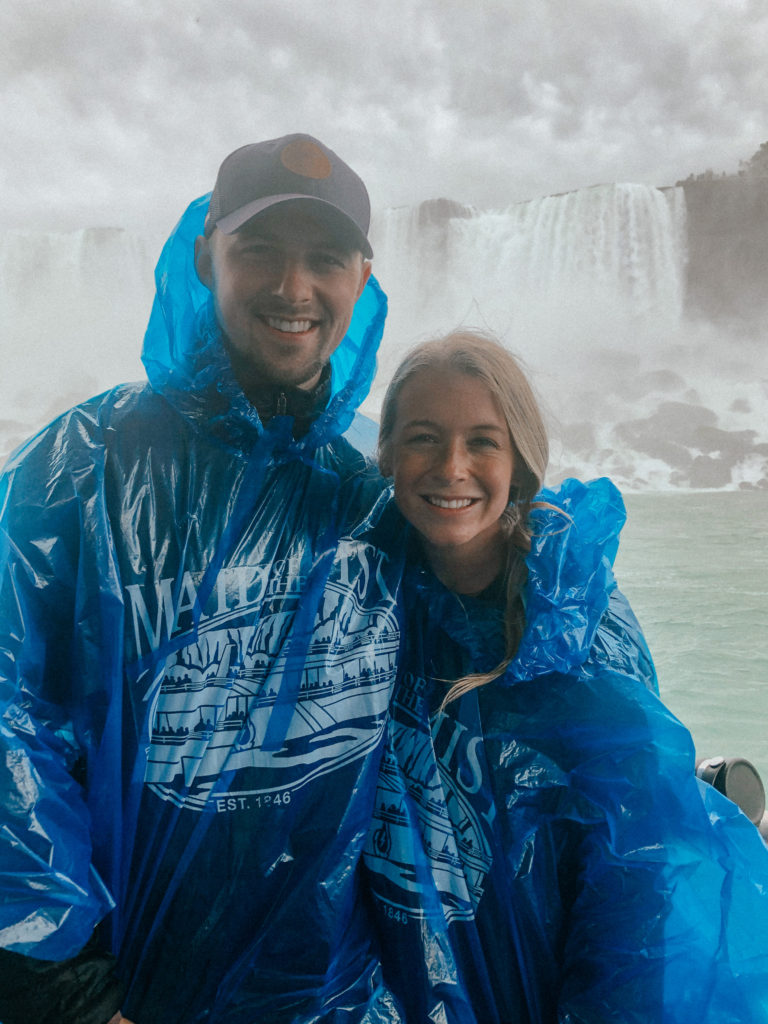 Sam and Abby smiling in blue ponchos with Niagara Falls roaring behind them.