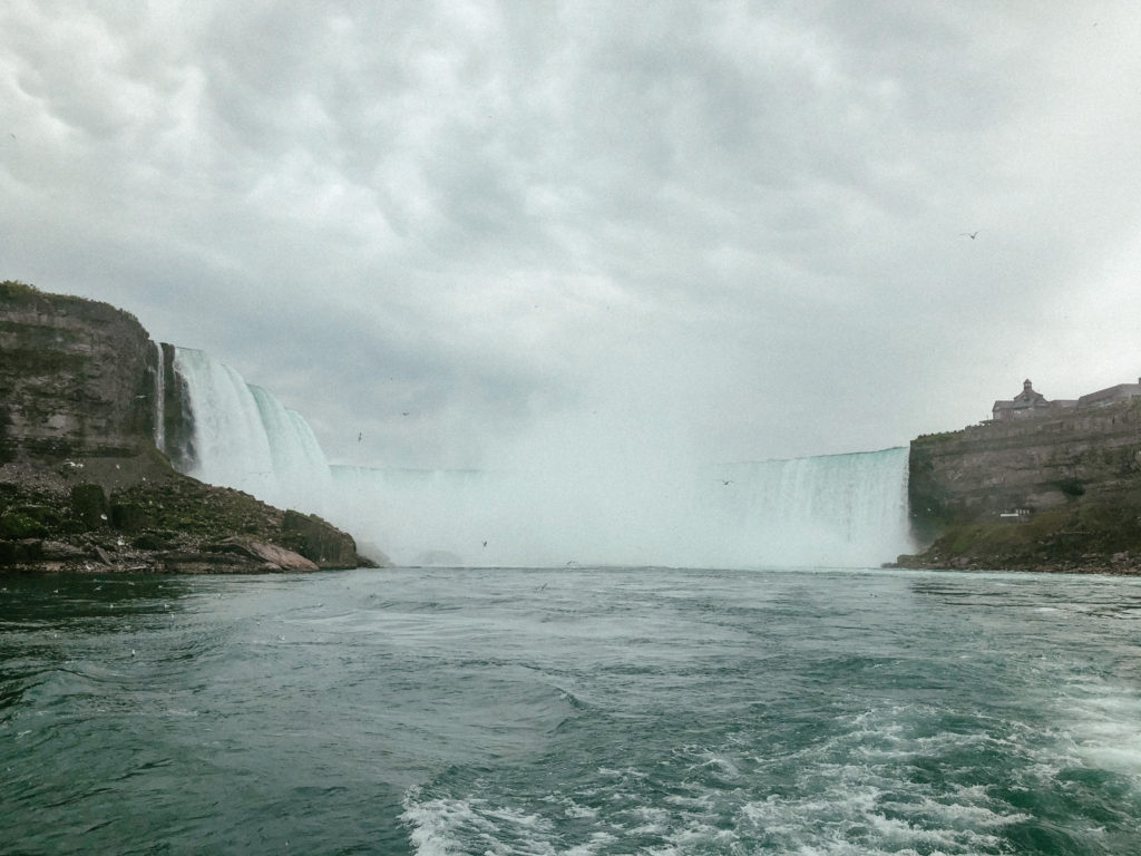 Niagara Falls gushing into the water down below with cloudy skies in the air.