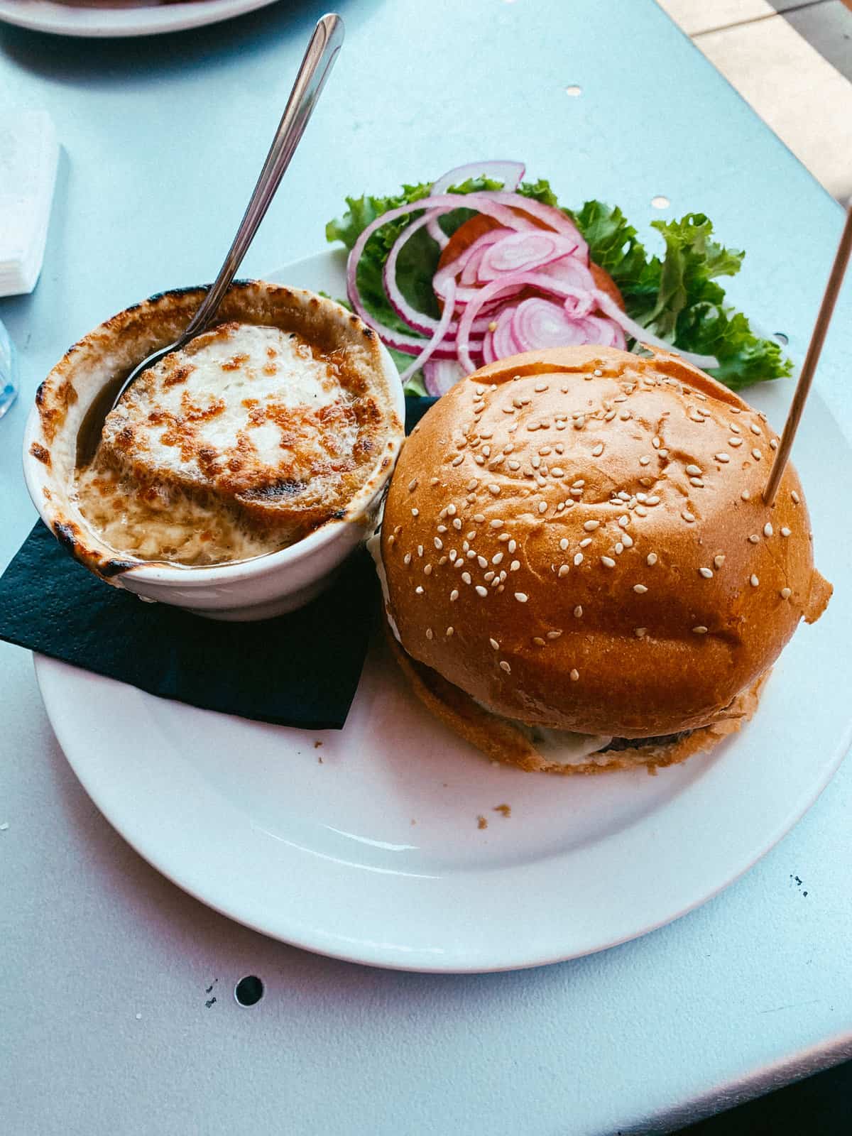 A cup of french onion soup and juicy burger.