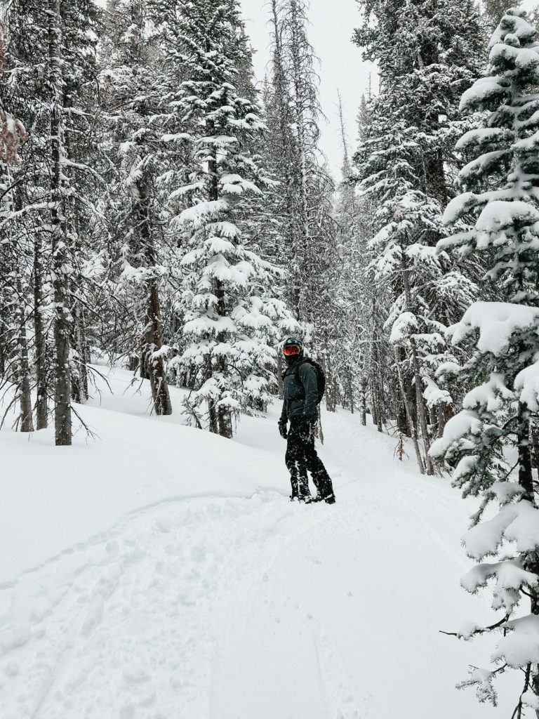 Sam snowboarding in Colorado surrounded by fresh powder and trees.