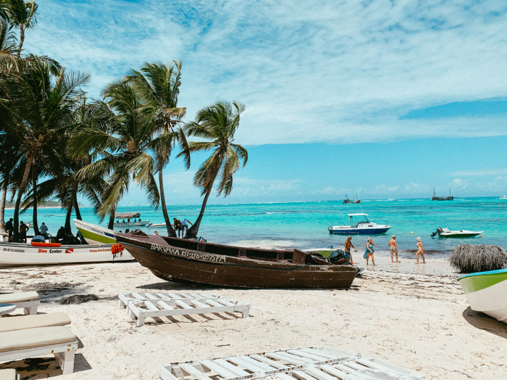 A boat on the sand in the Dominican Republic with a Dive Center boat behind it and palm trees and the ocean in the background.