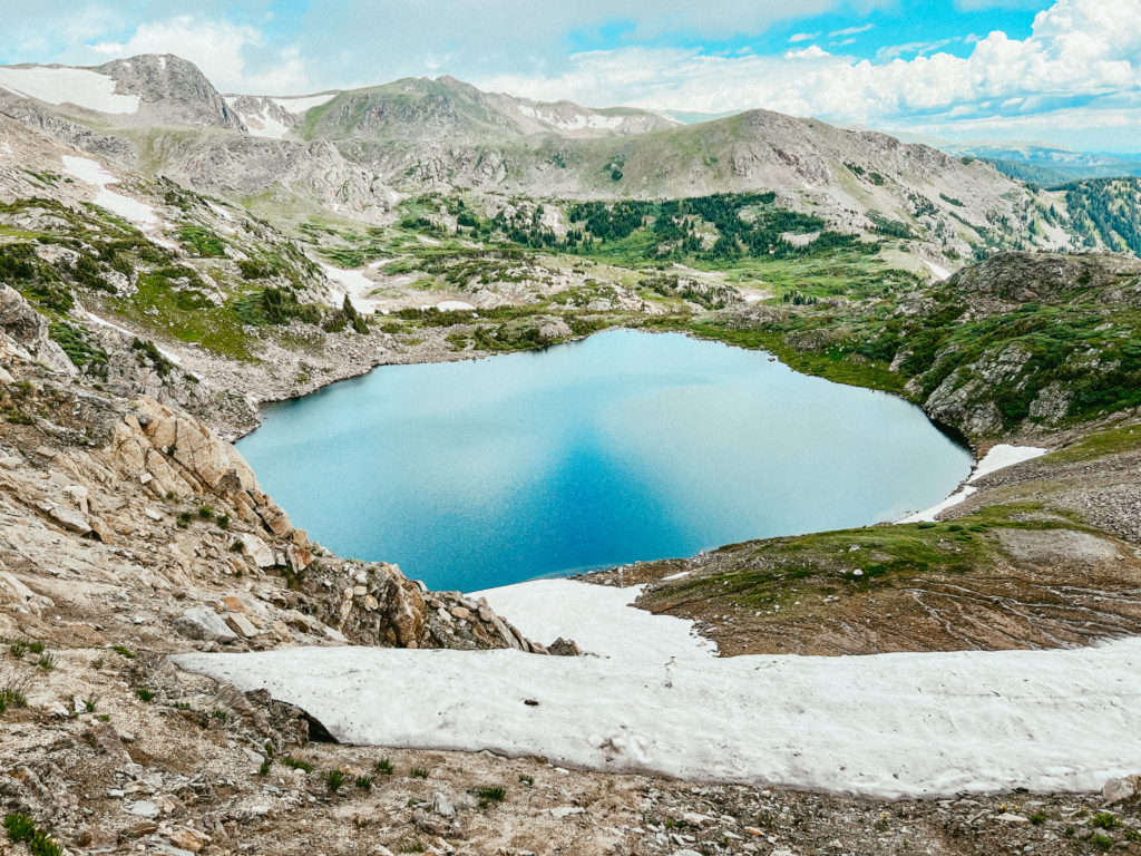 Mountains with snow and greenery surrounding an alpine lake in the center. 