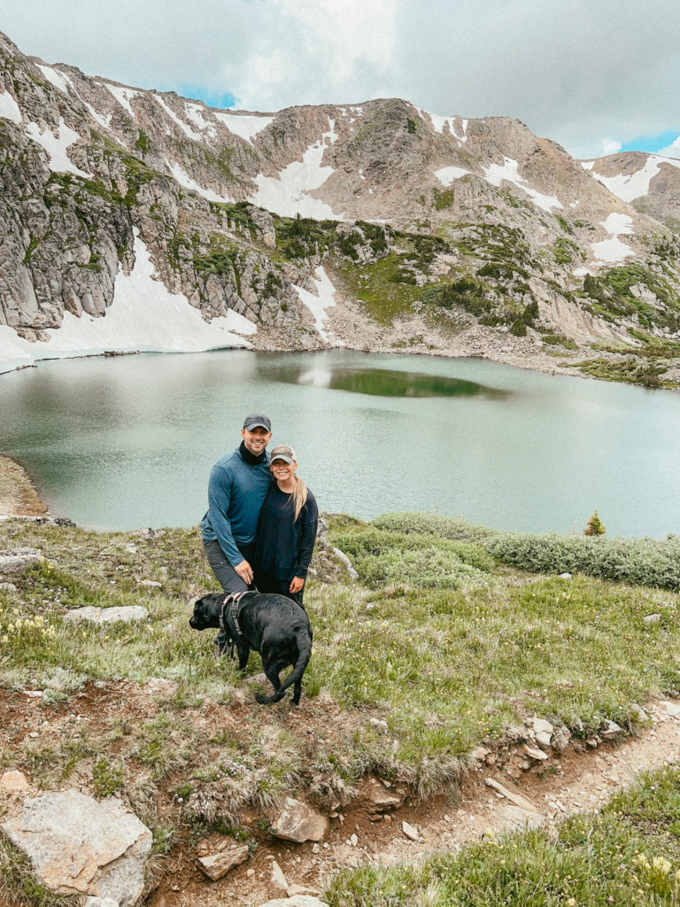 Abby, Sam, and Clover smiling on one of the best wilderflower hikes in Colorado with mountains and an alpine lake behind them.