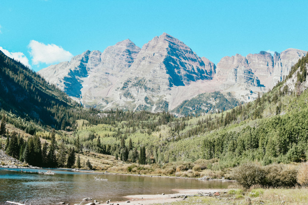 The Maroon Bells surrounded by greenery and a lake.