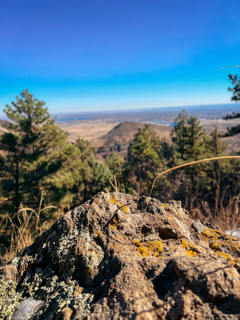 A view of a rock, green trees, and mountains in the distance with blue skies.