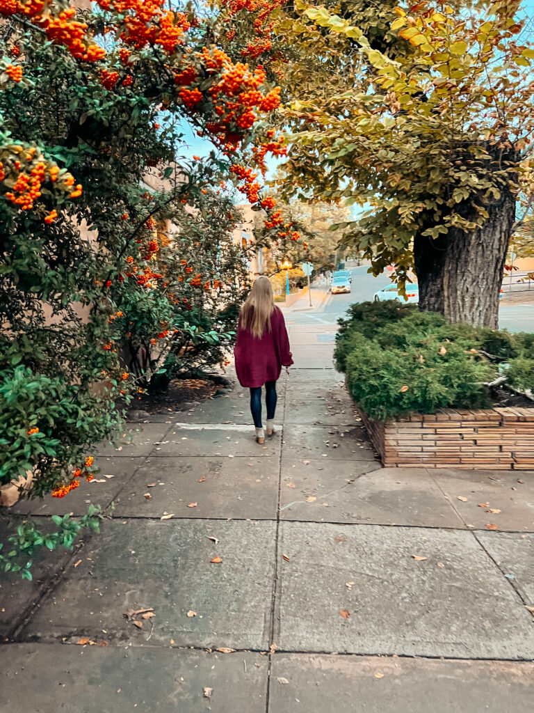 Abby walking down a street full of fall foliage where one of the best walking tours in Santa Fe takes place.