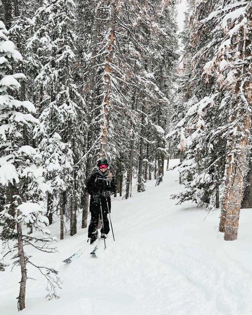 Abby skiing in Colorado surrounded by trees on a powder day.