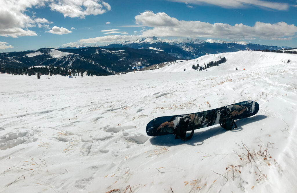 A snowboard laying on the snow with mountains in the distance.