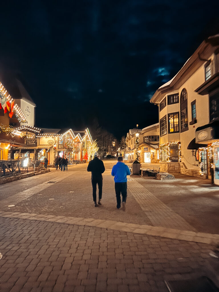 Two people walking down a ski village lit up at night on one of the best Colorado winter vacations for non skiers.