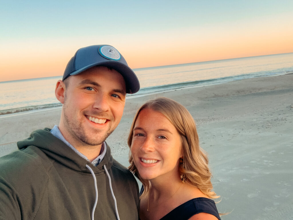Abby and Sam smiling on the beach during sunset.