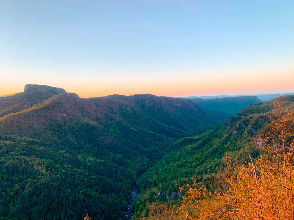 The sun setting over green mountains in North Carolina during a backpacking trip where Sam and Abby used some of the best hiking flashlights to help them navigate.