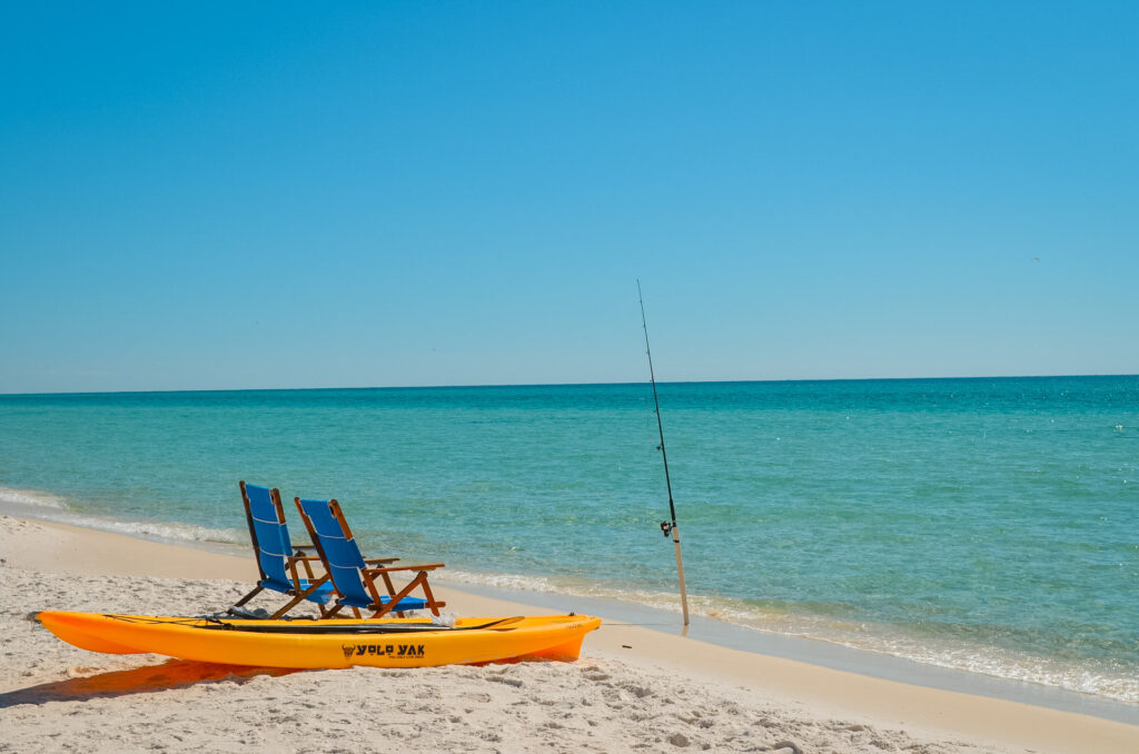 Two chairs and a kayak sitting beside a surf fishing rod set up with a rod holder.
