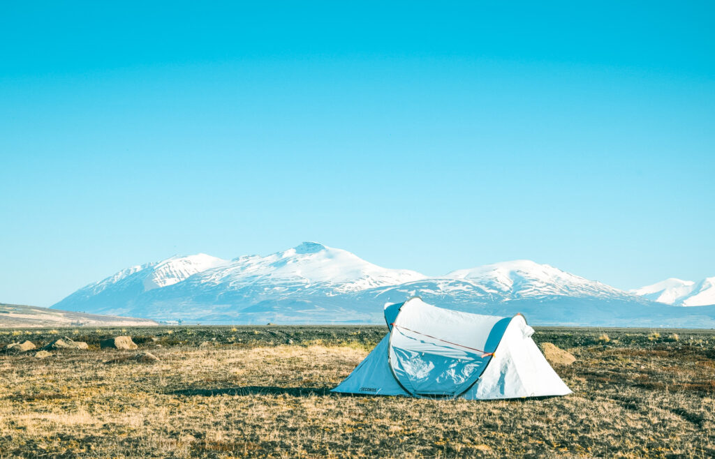 A tent pitched in the middle of grass with mountains in the distance.