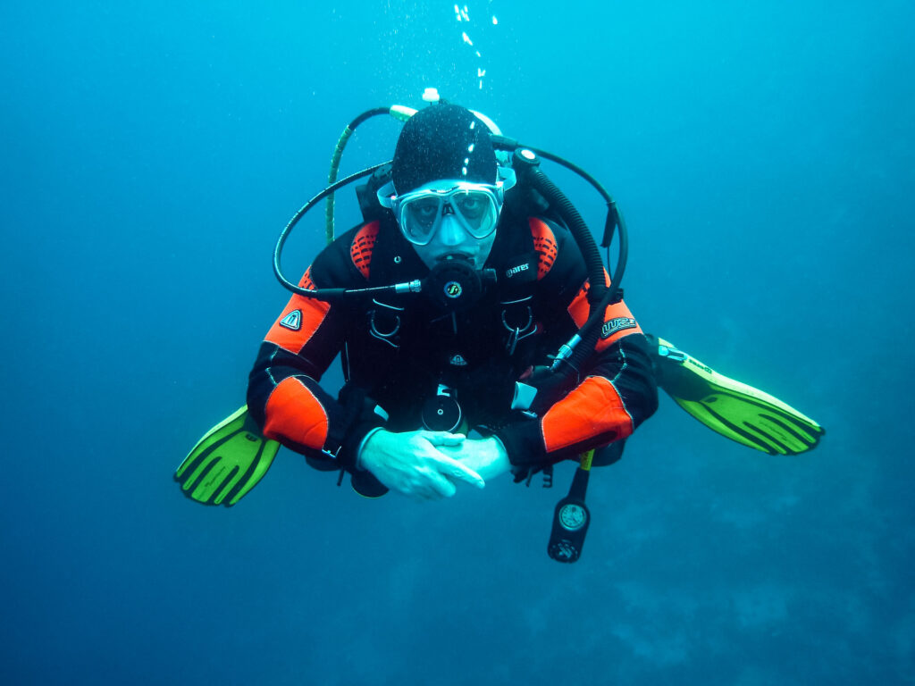 A scuba dive underwater wearing scuba gear, various equipment, and scuba fins. 
