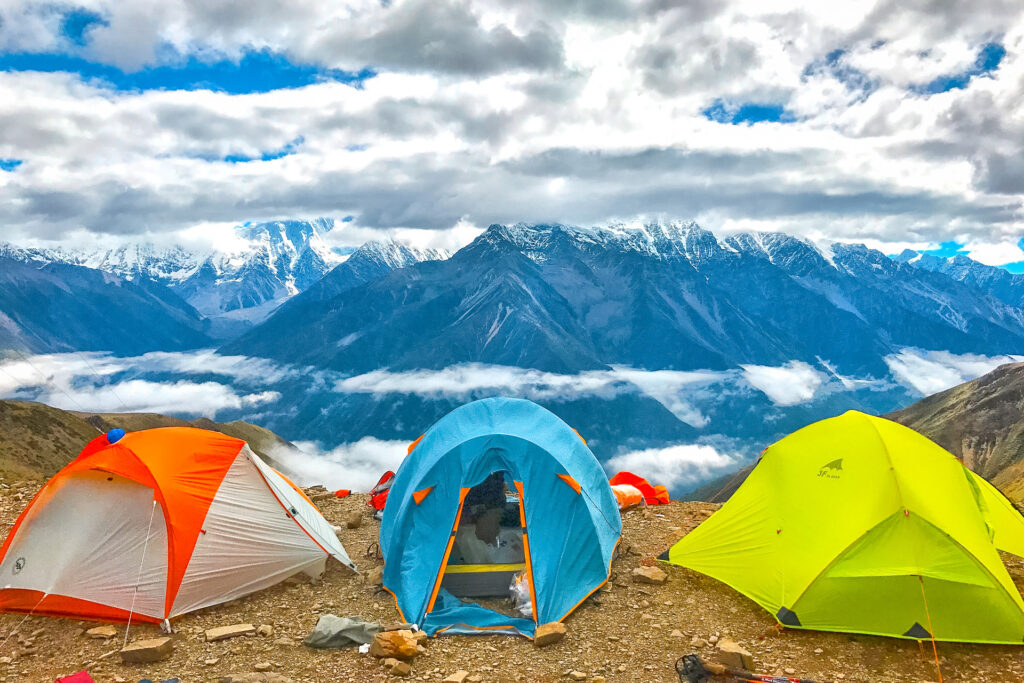 Three colorful tents set up with mountains and cloudy skies in the distance.