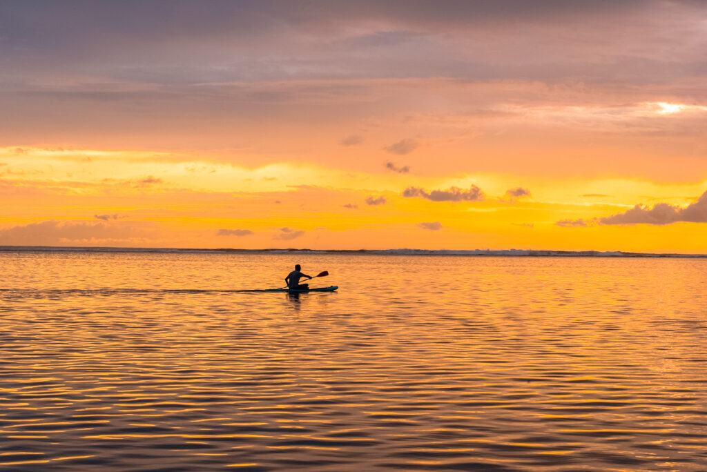 Someone kayaking on the open water during sunset.
