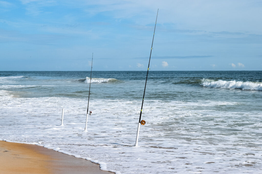 Surf fishing rods held up by rod holders as the ocean waves come in.