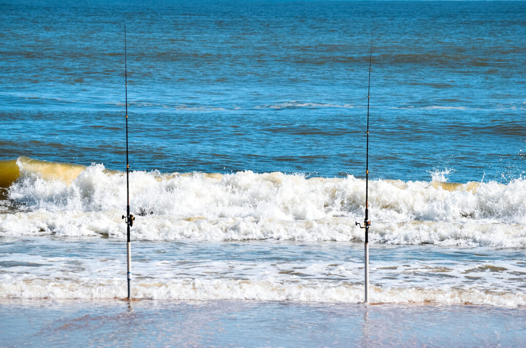 Two fishing rods held up by rod holders with the ocean in the distance.