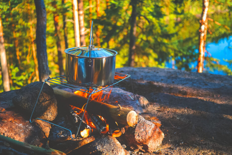 A stainless steel pot cooking on a foldable grill over top of a campfire. 