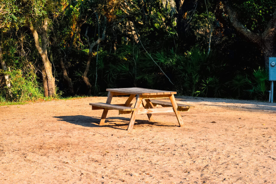 A picnic table set up on sand with green trees behind.