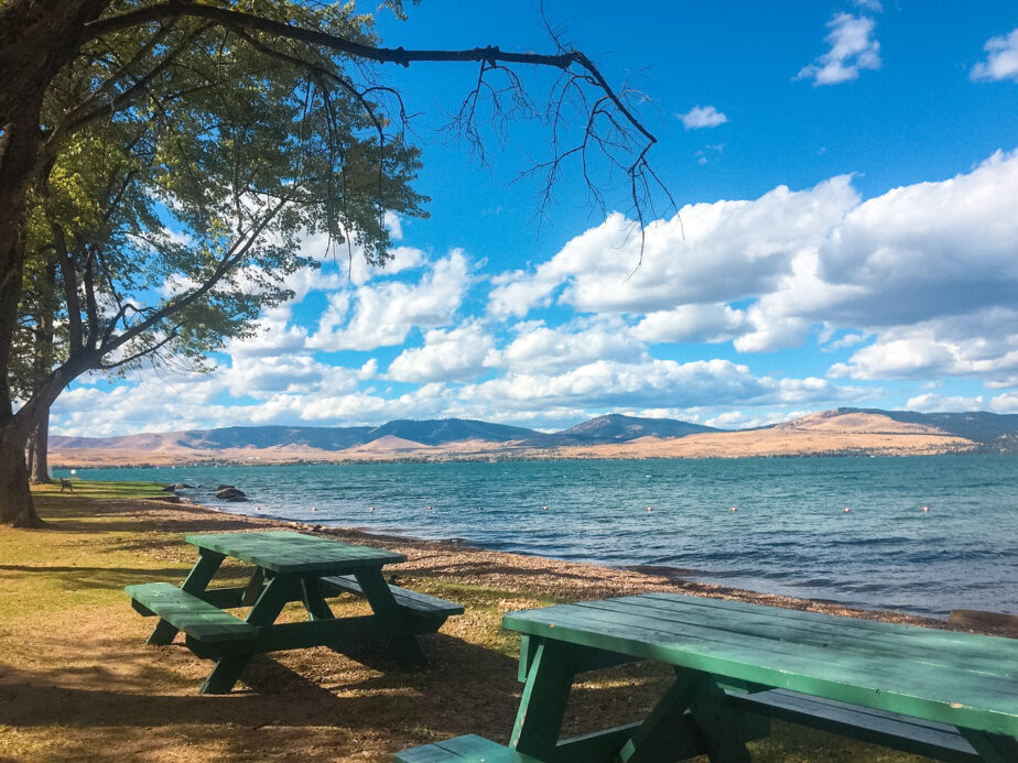 Picnic tables set up by the water with mountains in the distance.
