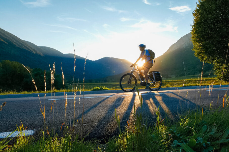 Someone riding a bike as the sun sets with mountains in the distance.