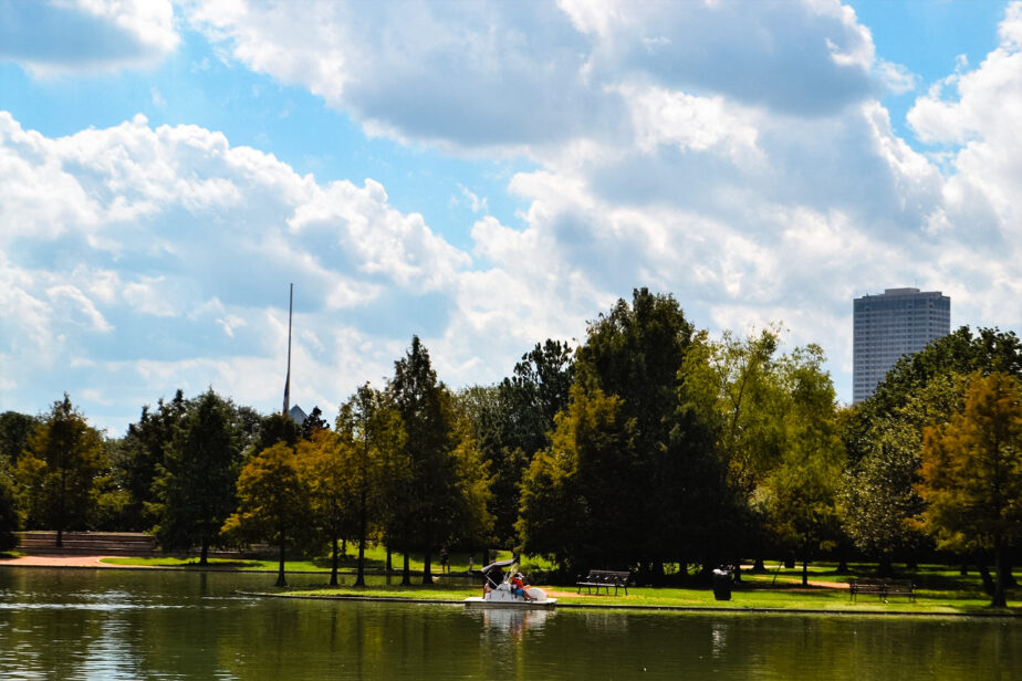 A park with a small lake and cloudy blue skies above.