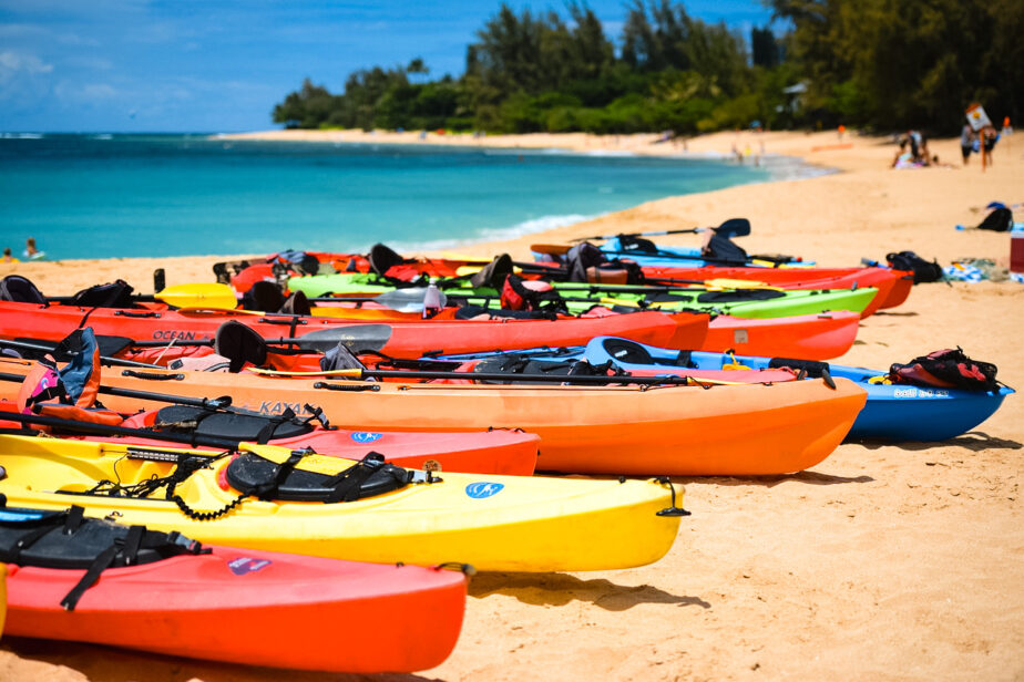 A fleet of colorful kayaks on the beach with the ocean in the background.