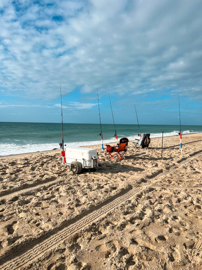 Surf fishing rods, a beach fishing cart, and one of the best saltwater tackle boxes set up on the beach in North Carolina.
