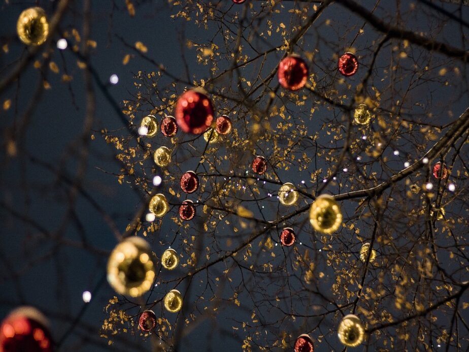 Christmas ornaments on a tree with lights outside.