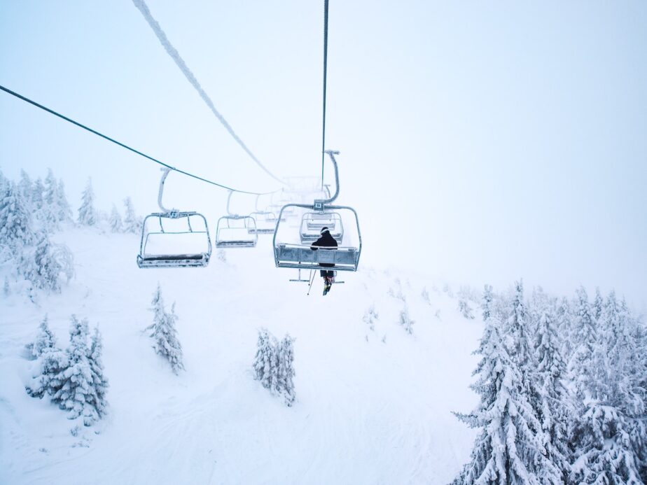 A skier sitting on a chair lift alone during a snowstorm.
