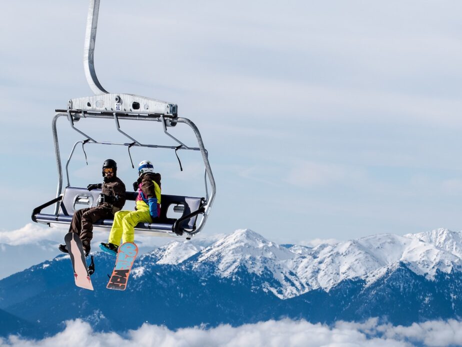 Two snowboarders sitting on a chair lift.