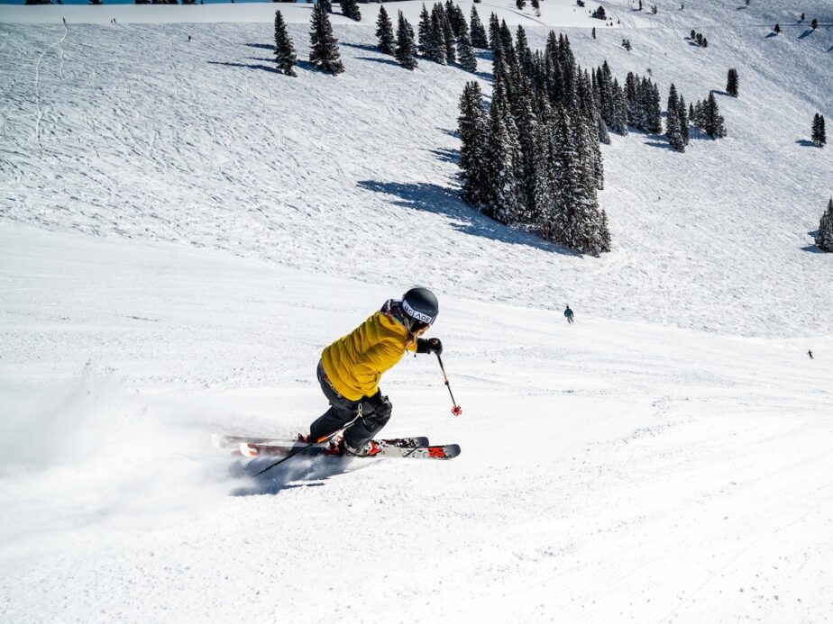 A skier in a yellow jacket going down a steep slope.