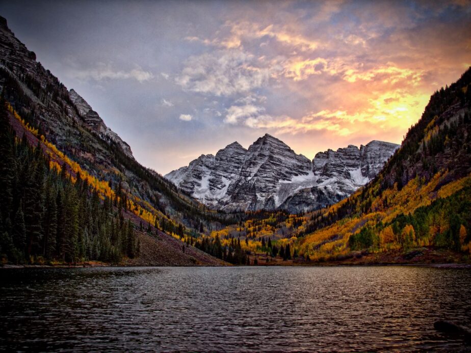 The Maroon Bells in Aspen with snow and trees surrounding them with fall foliage.