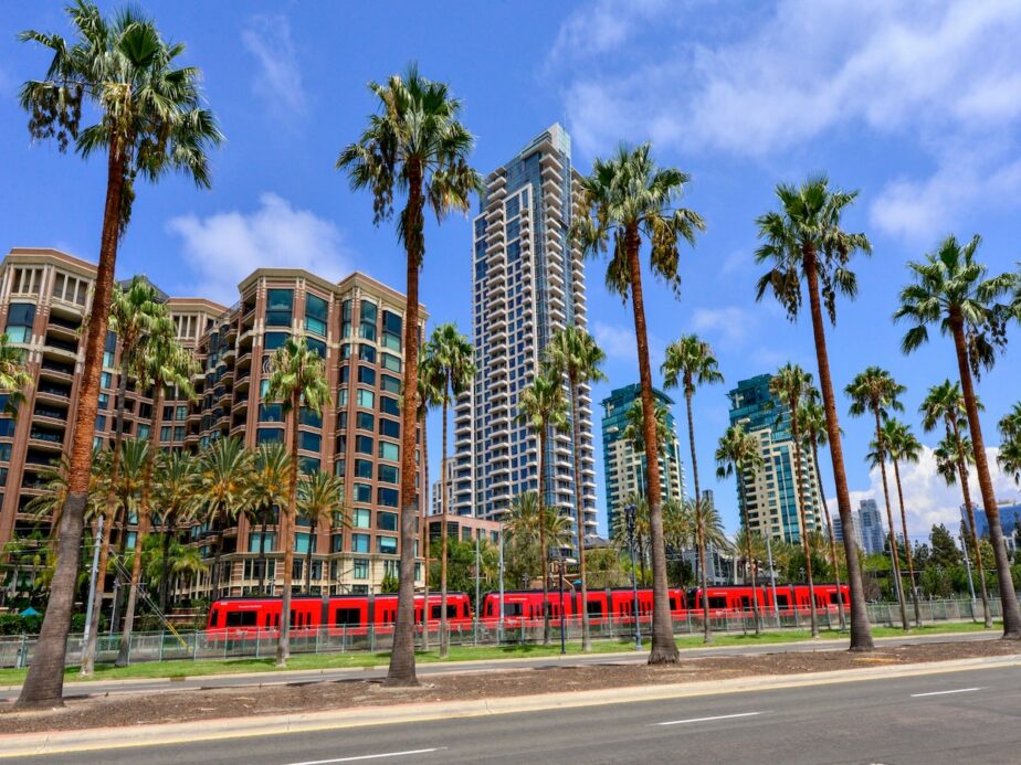 A bright red train surrounded by tall buildings and palm trees in San Fransisco. 