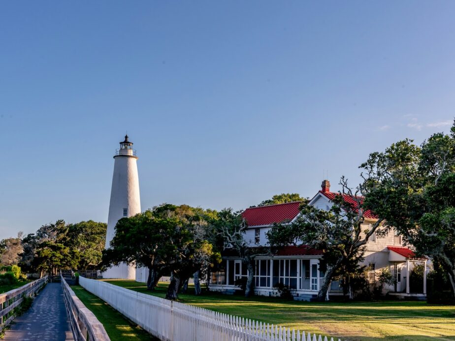 A lighthouse and building with a red roof on Ocracoke, one of the best places to visit in North Carolina in the summer.
