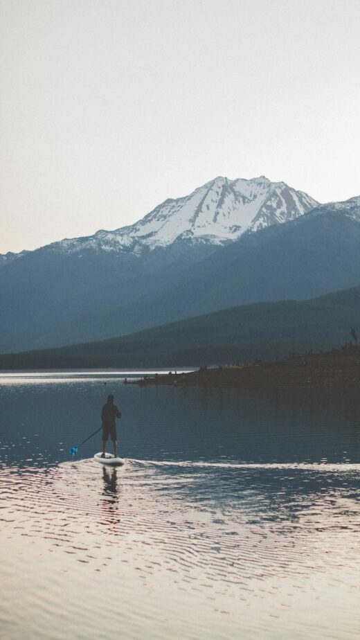 A person paddleboarding in Montana with a snowcapped mountain in the distance.