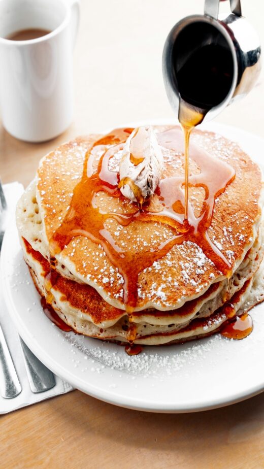 A stack of pancakes as the syrup is being poured on top of them.