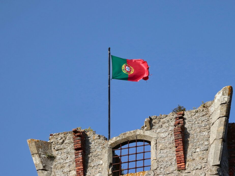 The Portugal flag flying in the wind above an old building.