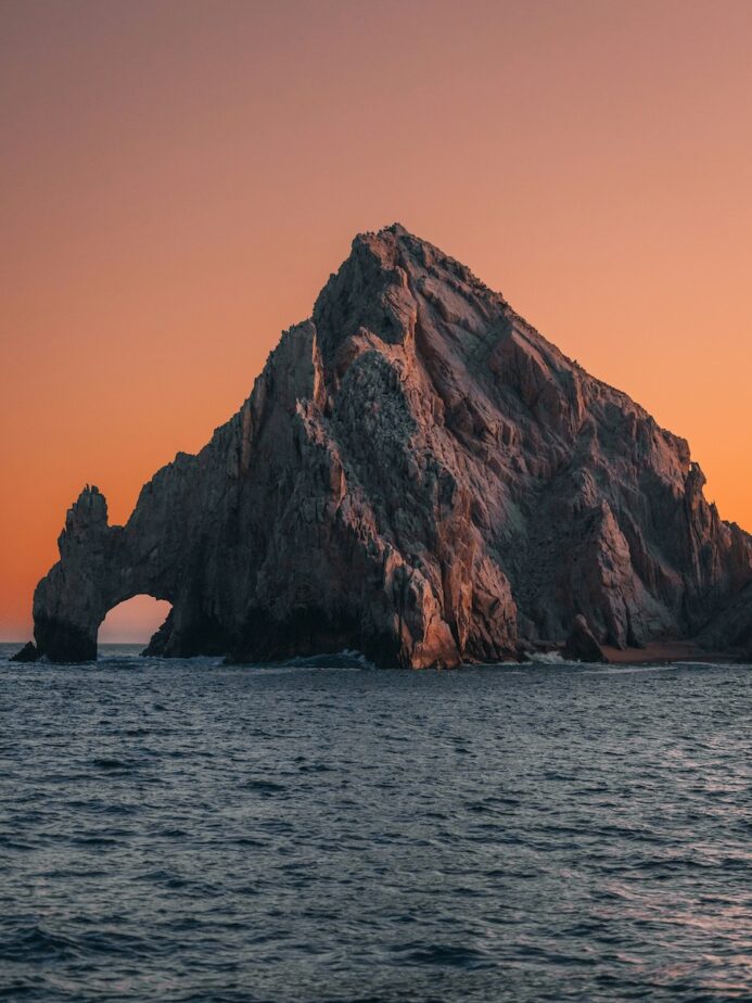 The sun setting over rocks and the ocean in Cabo San Lucas.