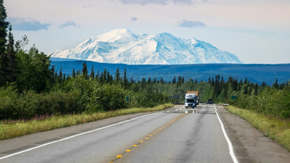 Cars along the Denali Highway with Denali covered in snow in the distance.